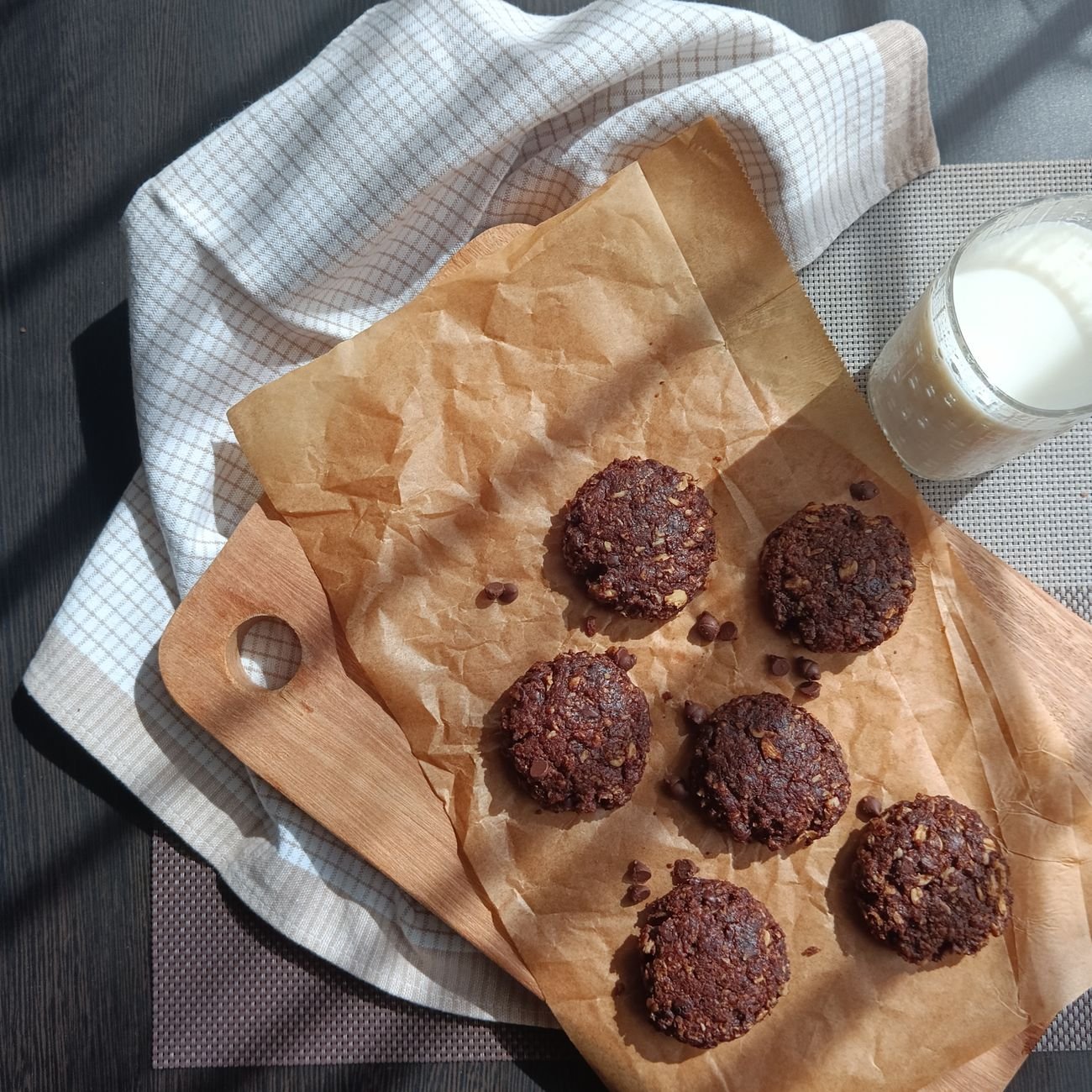 Top view of chocolate cookies on a wooden tray with a glass of milk, perfect for food photography.